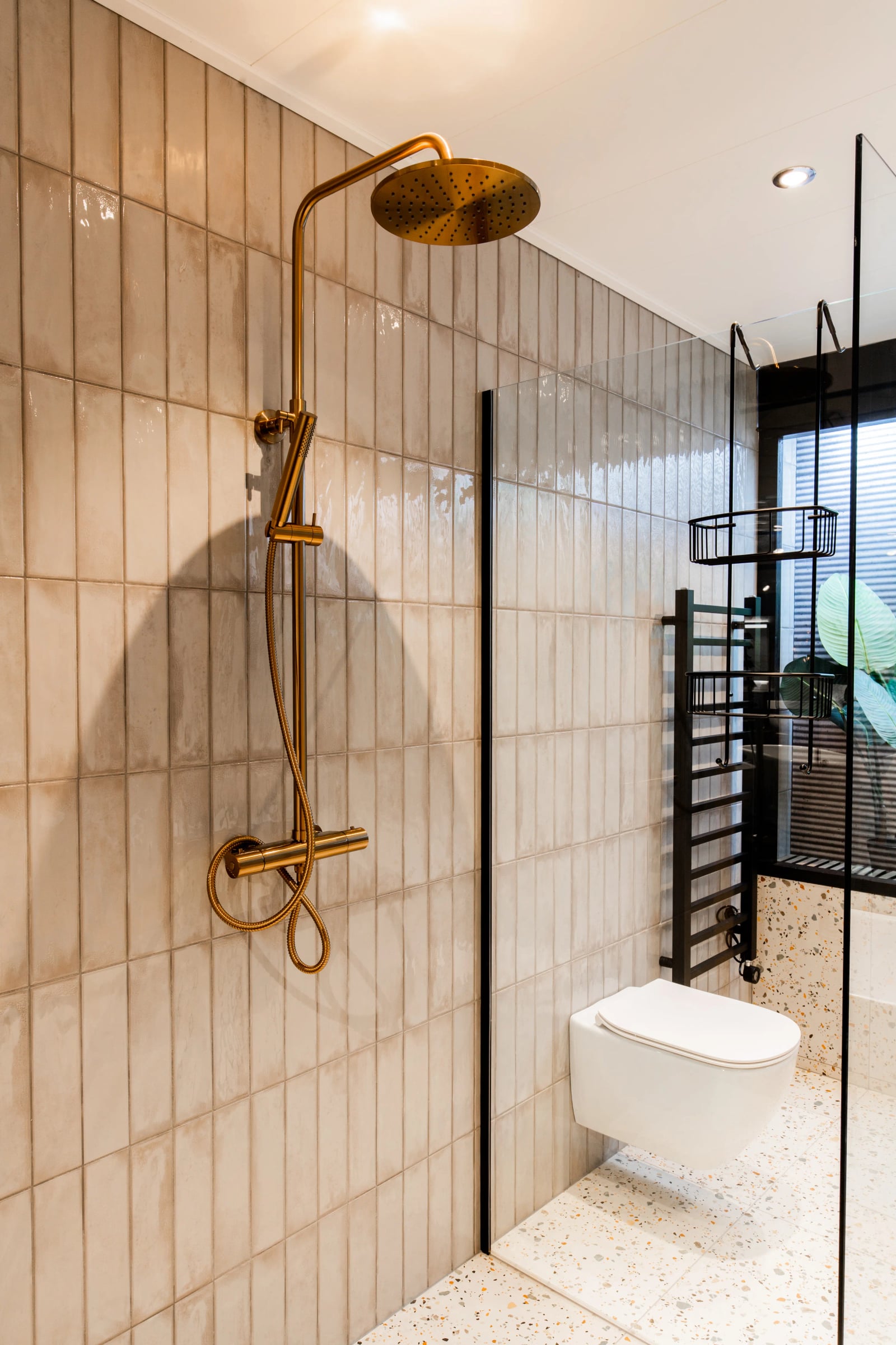 Badkamer van Homebleu met warme tegels en een gouden regendouche
